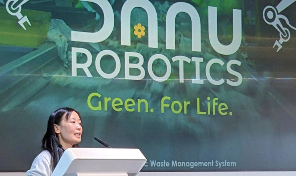 Woman speaking at podium in front of text "Danu Robotics. Green. For Life"