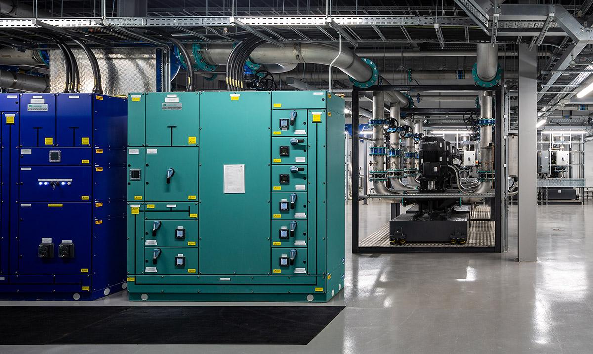 Photograph shows interior of computer facility with blue and green control units.