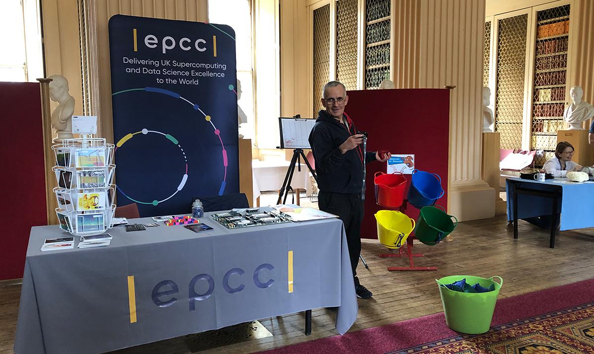 Science outreach stand with table and display banner, and man standing beside it looking at camera.