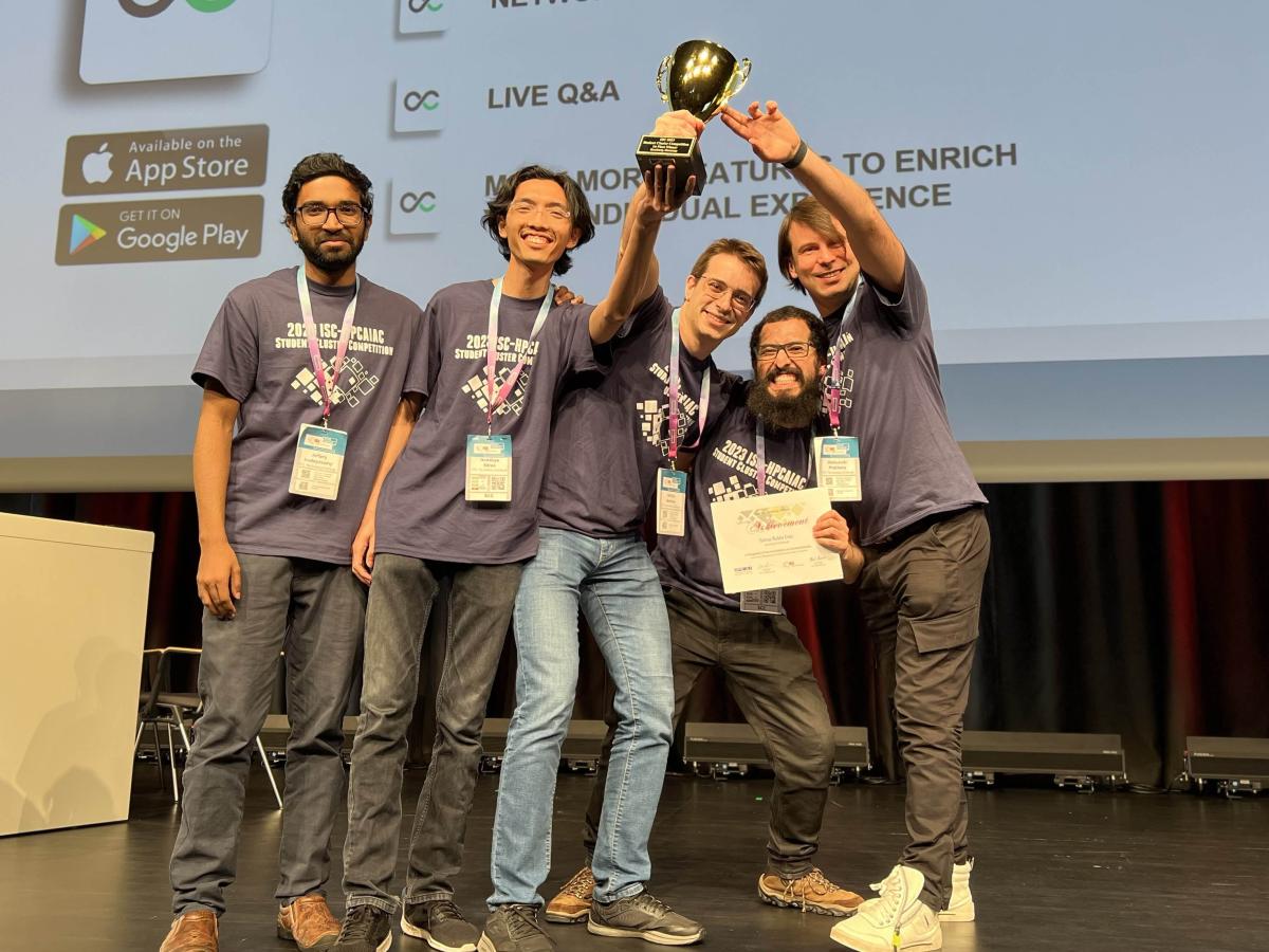 5 happy young men in jeans standing on a stage holding a gold winners cup