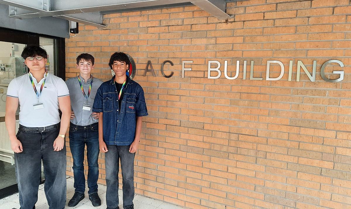3 older school pupils standing outside a brick building, with a sign "ACF Building".