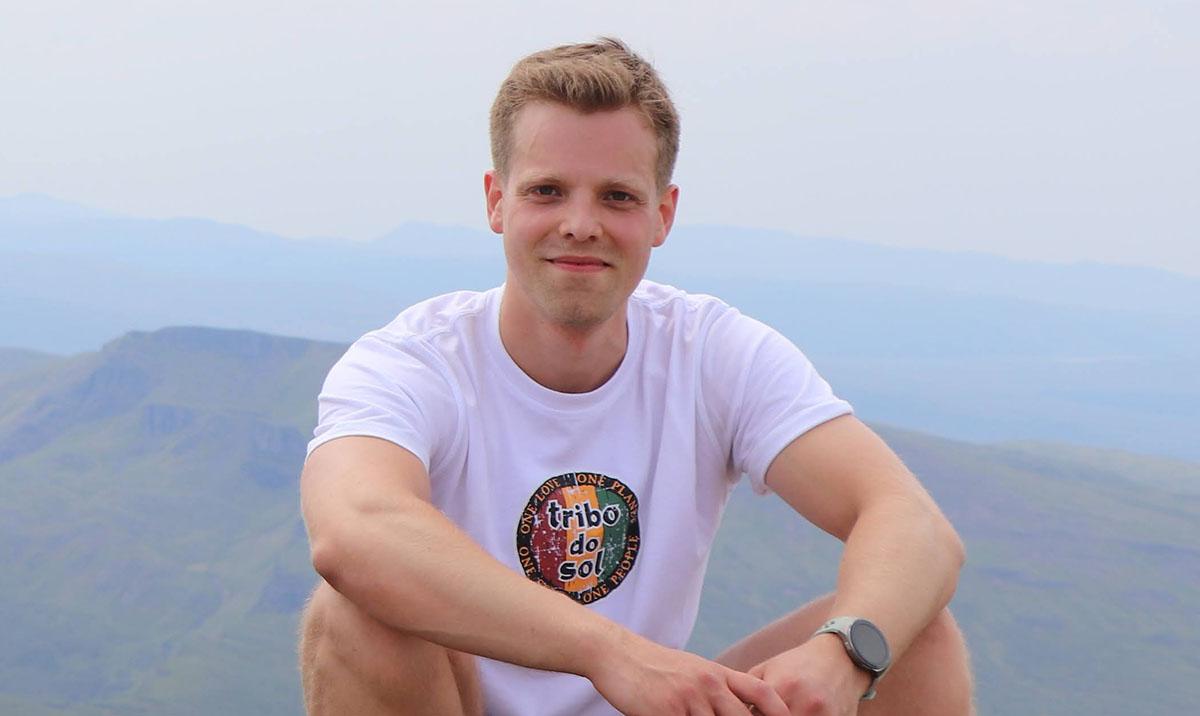 Young man sitting on hillside, facing camera.