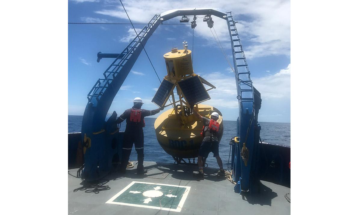 Photo of two men manoeuvring large equipment over side of ship at sea.