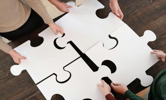 4 people, each holding a giant jigsaw piece. Image: Diva Plavalaguna at Pexels
