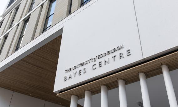 Phot showing front of Bayes Centre: flat white  panel carrying building title, supported by vertical columns beneath.