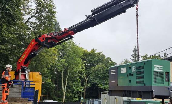 A crane lifts a generator from the back of a lorry