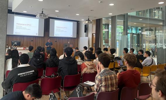 Photograph shows lecture theatre audience listening to male speaker.