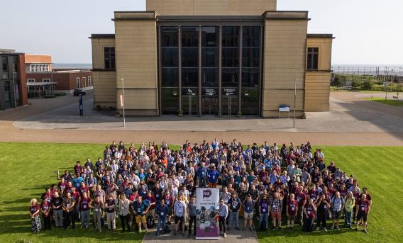 Aerial photograph of large group of people on lawn in front of conference centre