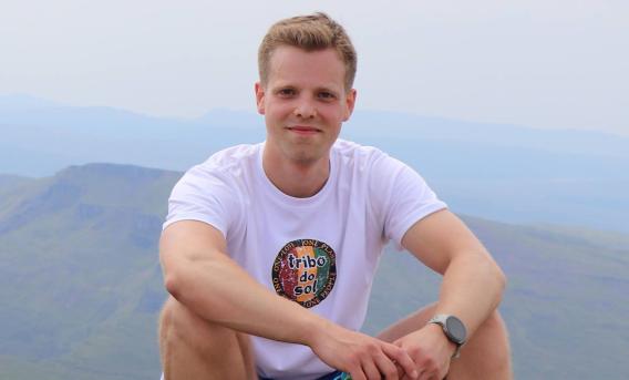 Young man sitting on hillside, smiling at camera