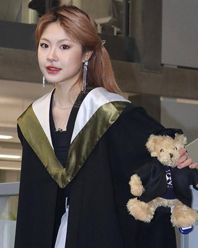 Young woman in graduation robe holding teddy bear